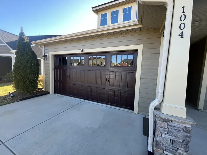 Completed Blackstone installation with a dark double garage door and upper windows on a white exterior
